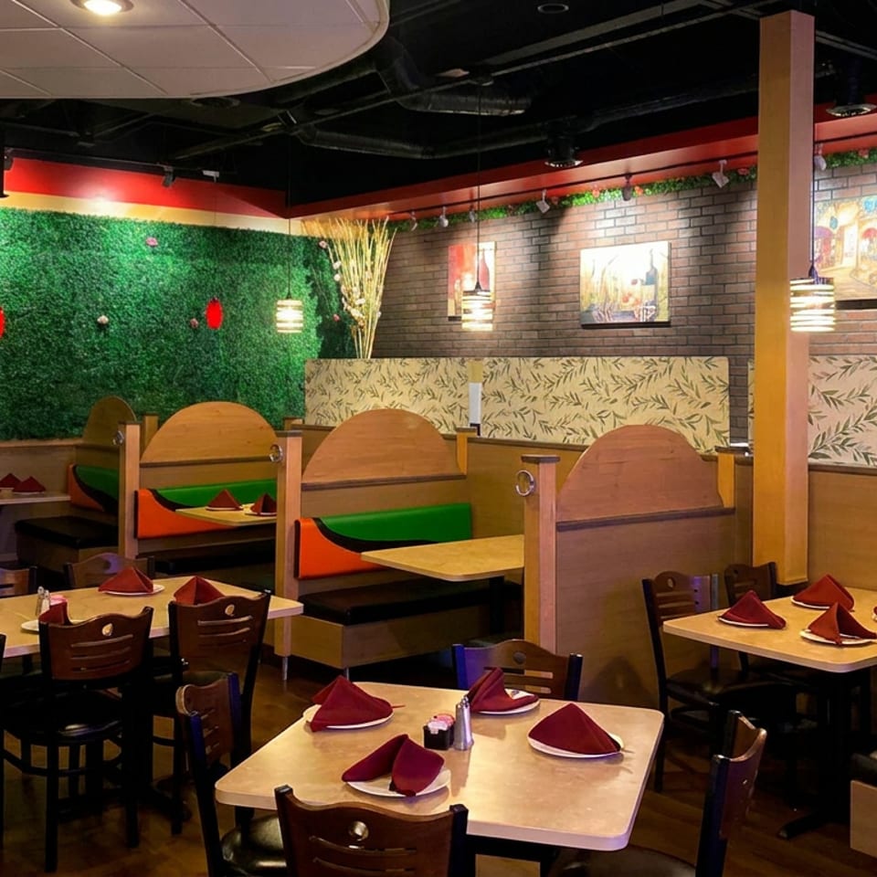 Colorful restaurant interior with booth seating, wooden tables, red folded napkins, decorative greenery, and brick walls.